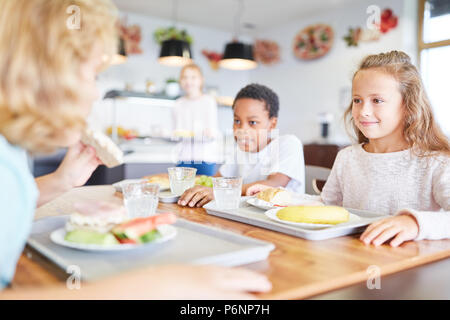 multiethnic kids having lunch in school canteen near teacher smiling on  blurred background Stock Photo - Alamy