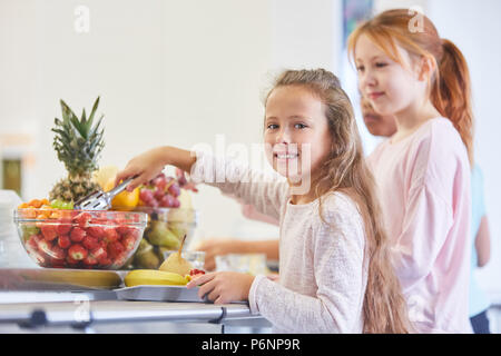 Girls and other children take fruits from the buffet in elementary school Stock Photo