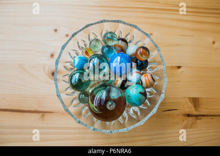 Colorful marbles in a bowl on wooden table. Stock Photo
