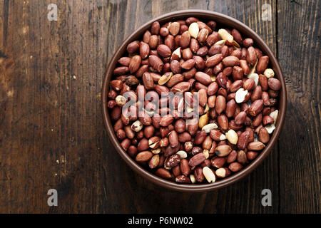 peanuts in a clay plate on a wooden background. place for text Stock Photo
