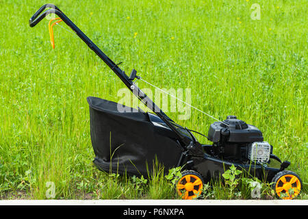 Modern gasoline powered lawn mower stands on fresh green grass, closeup photo, side view Stock Photo