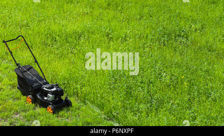 Modern gasoline powered rotary push mower or grass cutter stands on fresh green lawn Stock Photo