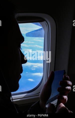 Closeup silhouette of young man using smartphone near window in airplane. Stock Photo