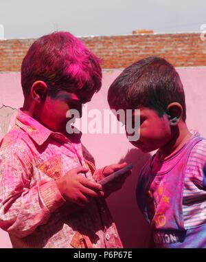 Close up of two cute little Indian boys covered in Holi coloured powder looking at a mobile phone (cellphone) Stock Photo