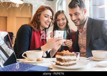 Three young friends using a mobile phone for fun during a coffee break Stock Photo