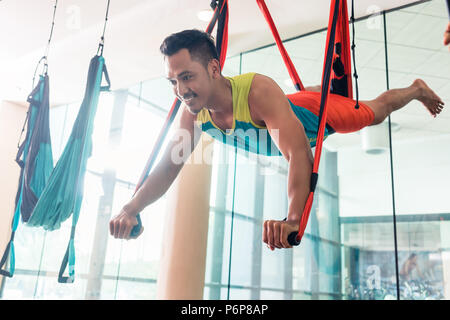 Fit handsome man smiling while practicing anti-gravity yoga Stock Photo