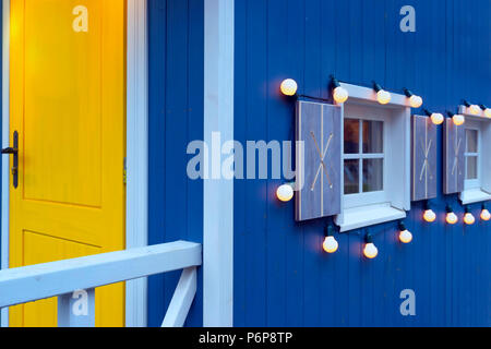 Windows with light bulbs on a blue painted wooden house wall with a yellow door Stock Photo