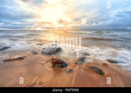 Autumn sunset with waves on the yellow sandy beach of the Baltic with large stones and ice Stock Photo