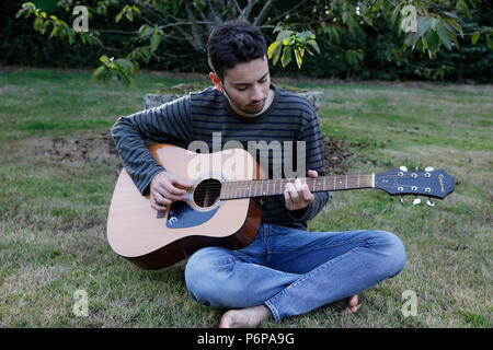 Young man playing a guitar in a garden. France. Stock Photo