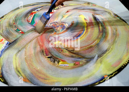 A Tibetan monk uses a paint brush to blend colored sand mandal and sweep it into a pile. Stock Photo