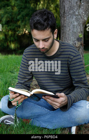 Young man reading the Kuran in a park. France. Stock Photo