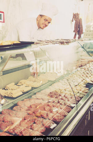 Happy shop-boy in working clothes taking raw meat from stall Stock Photo
