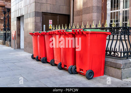 A row of 6 red wheelie bins on the pavement in a street in Manchester City Centre, UK Stock Photo