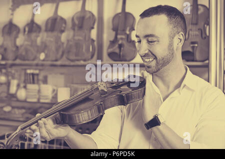 Cheerful man with beard purchasing traditional violins in store Stock Photo