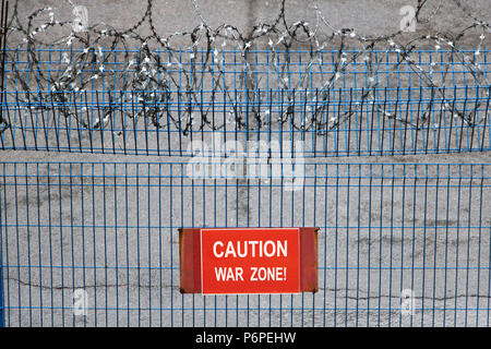 Iron fence with barbed wire. Metallic fence with red warning sign War zone! Stock Photo