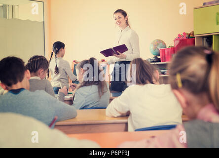Positive friendly  diligent pleasant female teacher standing at blackboard with schoolgirl during lesson in classroom Stock Photo