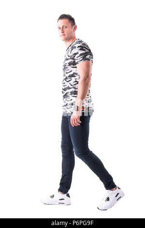 Young adult stylish man in military style t-shirt walking and looking at camera. Side view. Full body isolated on white background. Stock Photo