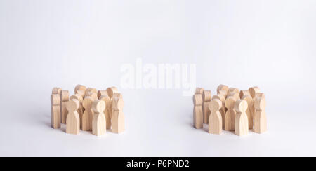 Two crowds of wooden figures of people are standing on a white background. The concept of different social groups, the opposition of ineters, the divi Stock Photo