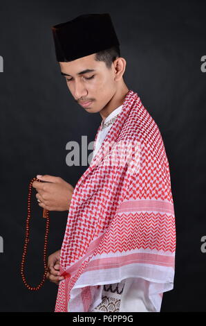 Young asian muslim man praying with prayer beads Stock Photo