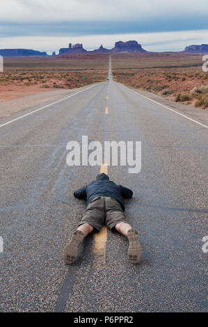 Man lying flat on his belly to take a picture of Highway 163 leading to Monument Valley, Arizona, USA. Stock Photo
