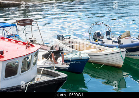 Burtonport, County Donegal, Ireland weather. 2nd July 2018. The warm weather continues with a cooling breeze in the harbour on Ireland's north-west coast. A man takes advantage of the hot day to fix his boat. Credit: Richard Wayman/Alamy Live News Stock Photo