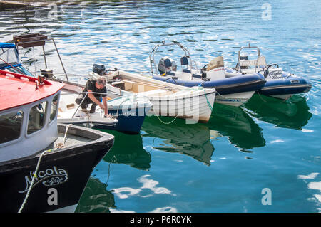 Burtonport, County Donegal, Ireland weather. 2nd July 2018. The warm weather continues with a cooling breeze in the harbour on Ireland's north-west coast. A man takes advantage of the hot day to fix his boat. Credit: Richard Wayman/Alamy Live News Stock Photo