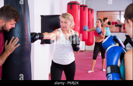 mature female is doing exercises with punching bag in sporty gym Stock Photo