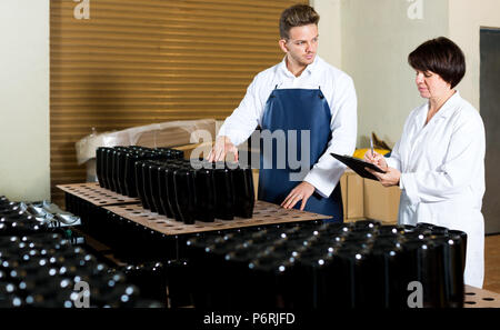 Glad employees checking number of wine bottles at sparkling wine factory Stock Photo
