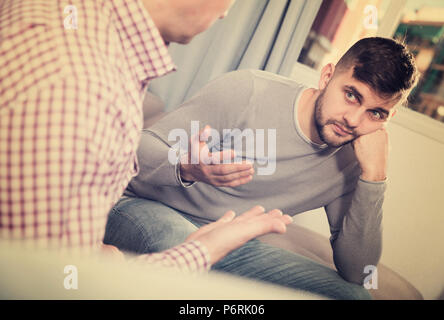 Upset man having unpleasant talk with male colleague on couch in home interior Stock Photo