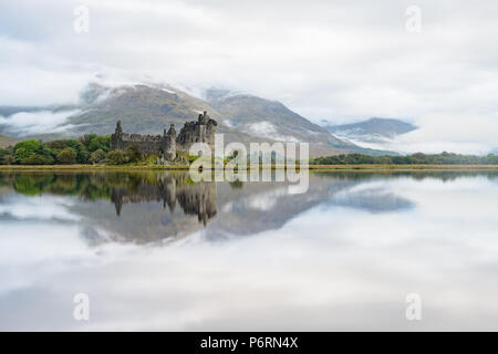 Reflections of Kilchurn Castle in Argyll and Bute, Scotland, in the calm waters of Loch Awe and surrounded by rolling mist from the Cruachan hills Stock Photo