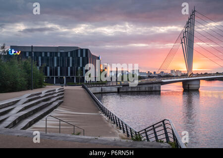 Colourful setting sun over water and Calatrava-style bridge in an urban environment at Salford Quays in Manchester, UK, showing the ITV studios Stock Photo