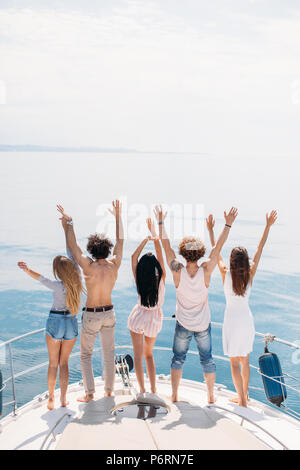 Rear view of cheerful caucasian teenagers on a sailing boat, lifting their hands up, looking at blue sea surfice, full of happiness,celebrating the st Stock Photo