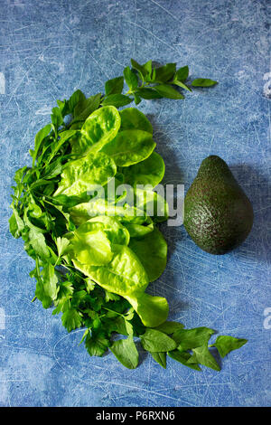 Fresh ripe avocado and various herbs, lettuce, basil, parsley and spinach on a blue background. Stock Photo
