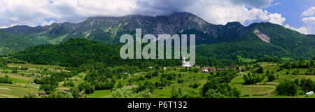 Beautiful panoramic view over a green valley with a small village in the Slovenian countryside with mountains and a cloudy sky in the background Stock Photo