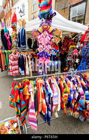 Racks and hangers full of multi-coloured clothing at market stall. Wide angle view, clothing filling frame. Stock Photo