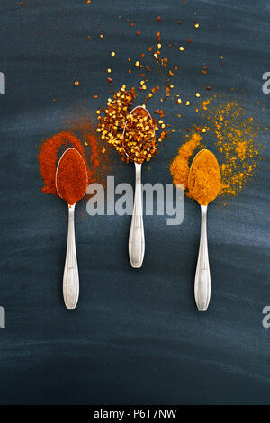 Vintage silver spoons full of paprika, turmeric and chili flakes on a dark background Stock Photo