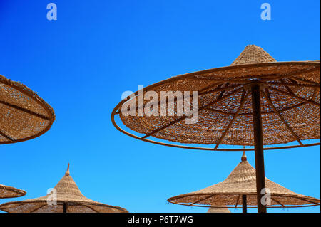 sun-protecting wicker umbrellas on the beach against the sky, the concept of summer tourism Stock Photo