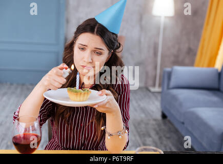 Dark-haired woman burning candle on little birthday muffin Stock Photo