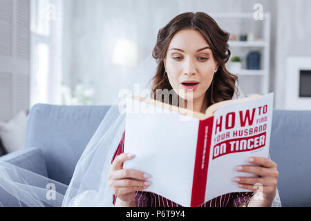 Dark-eyed woman feeling curious while reading book Stock Photo