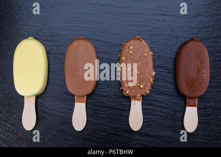 Ice cream on stick covered with chocolate on black stone slate board. Stock Photo