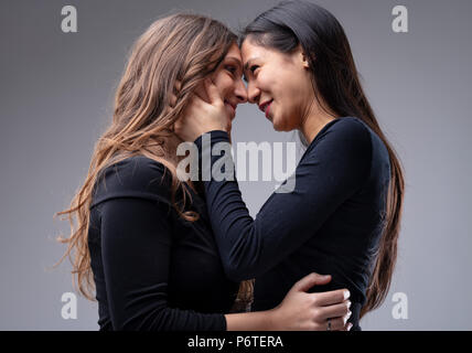 couple of young women holding each other on the hips and the face looking each other right in the eyes and smiling like just before a kiss Stock Photo