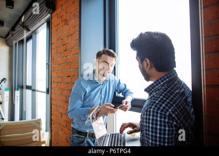 Two multiracial colleagues discussing last evening spending together in pub, standing at the window during lunch break Stock Photo