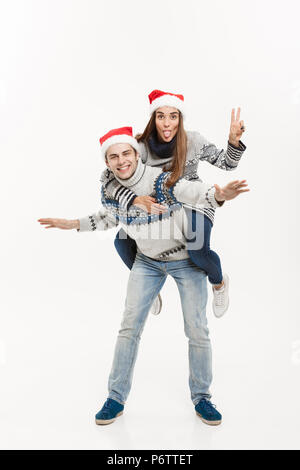 Christmas Concept - Young happy couple in sweaters enjoying piggyback ride isolated on white grey background Stock Photo