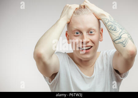 Emotional overjoyed Albino hipster guy with bugged eyes and open mouth grabbing his hair in disbelief and happyness with tattooed hands. Human emotion Stock Photo