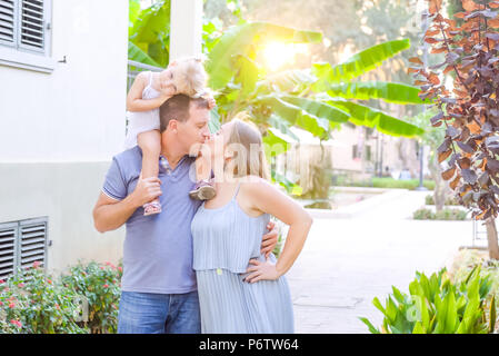 Happy family of three - pregnant mother, father and daughter hugging, laughing, having fun in the sunset park. Family recreation, spending time togeth Stock Photo