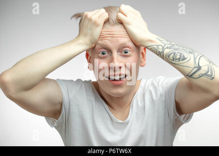 Expressive overjoyed shocked surprised Albino male model holding head with tattooed arms and looking at camera with bugged eyes and open mouth. Human  Stock Photo