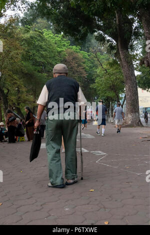 Elderly man walking, with the aid of a walking stick, around the legendary Hoan Kiem Lake, Hanoi, Vietnam Stock Photo