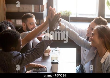 Multiracial friends giving high five sitting out in coffee shop Stock Photo