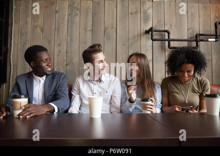 Smiling multiracial friends drinking coffee having fun in cafe