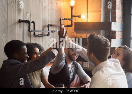 Smiling millennials giving high five during meeting in cafe Stock Photo
